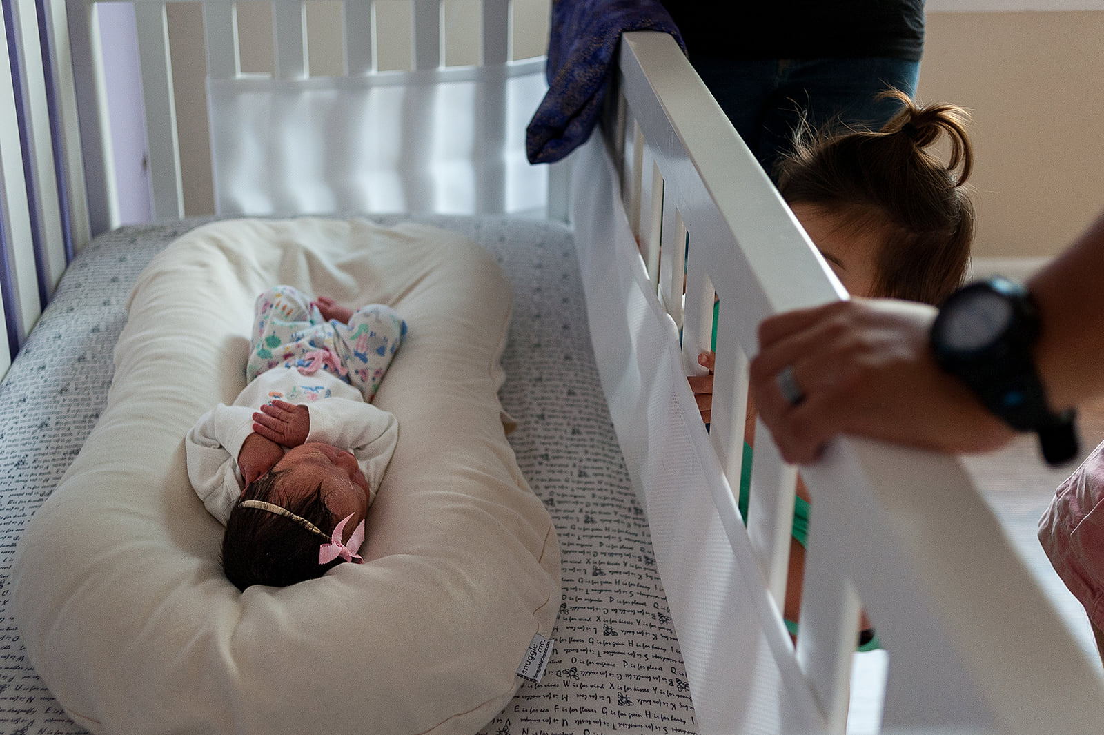Annabelle peeks through crib at her baby sister.