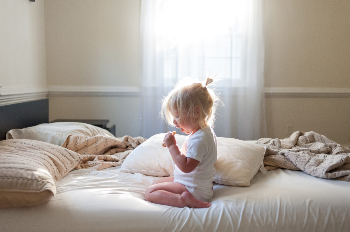 girl sitting on bed enjoying delicious chocolate chip cookie.