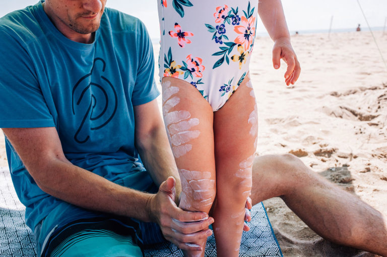 Dad puts sunscreen handprints on daughters legs.