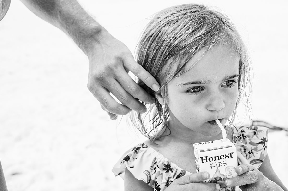 Girl drinks Honest Kids juice on beach.