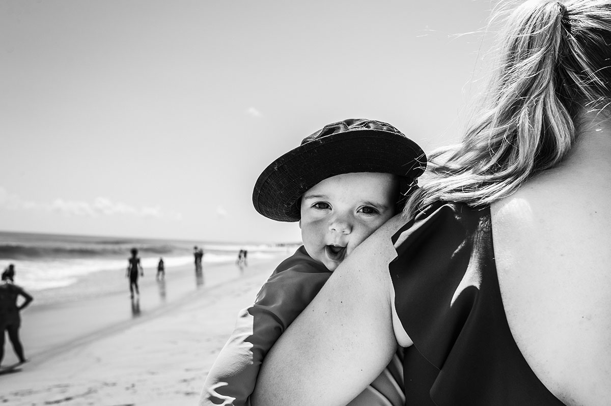 Mom holds smiling baby with sun hat on.