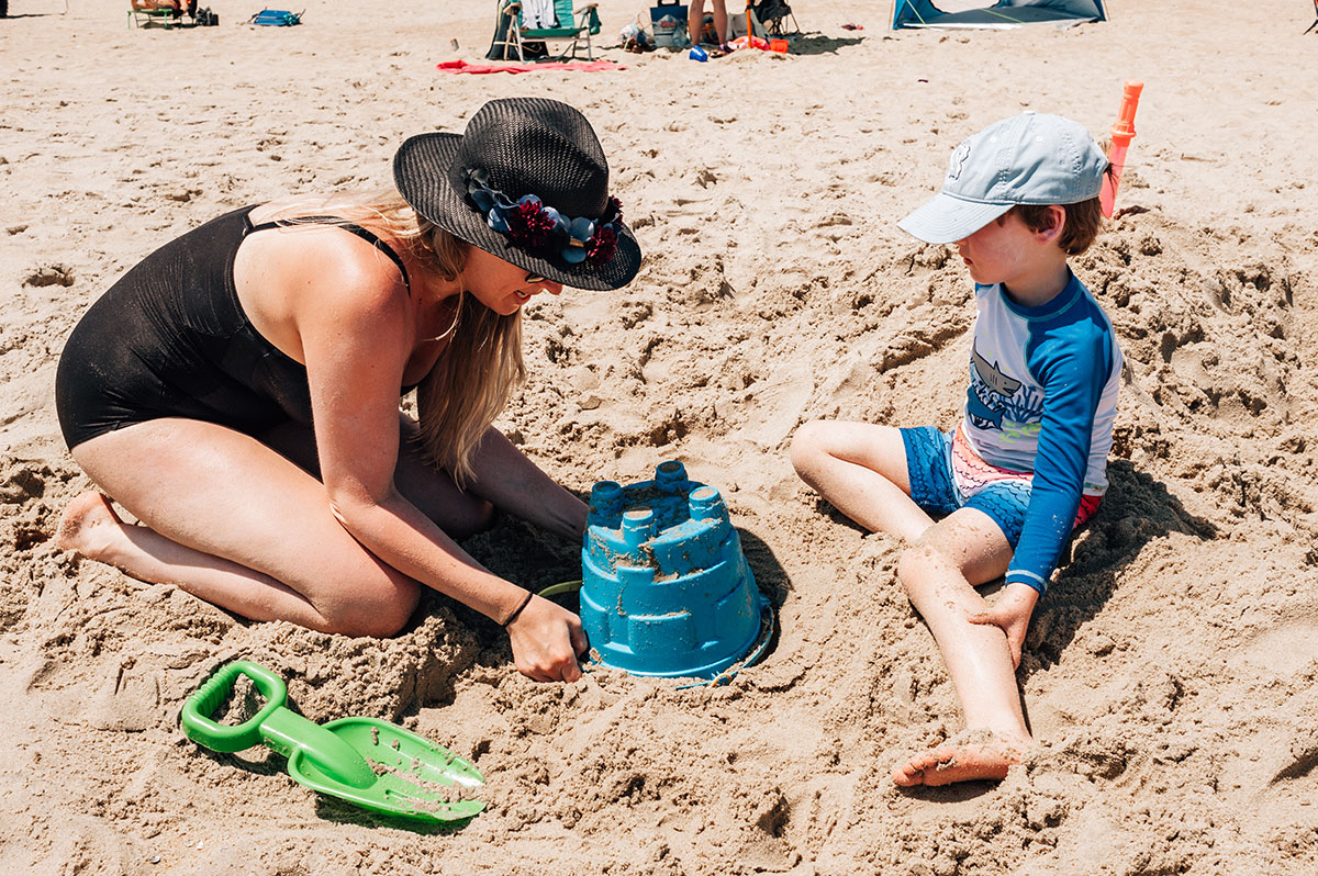 mom helping son build sand castle on the beach
