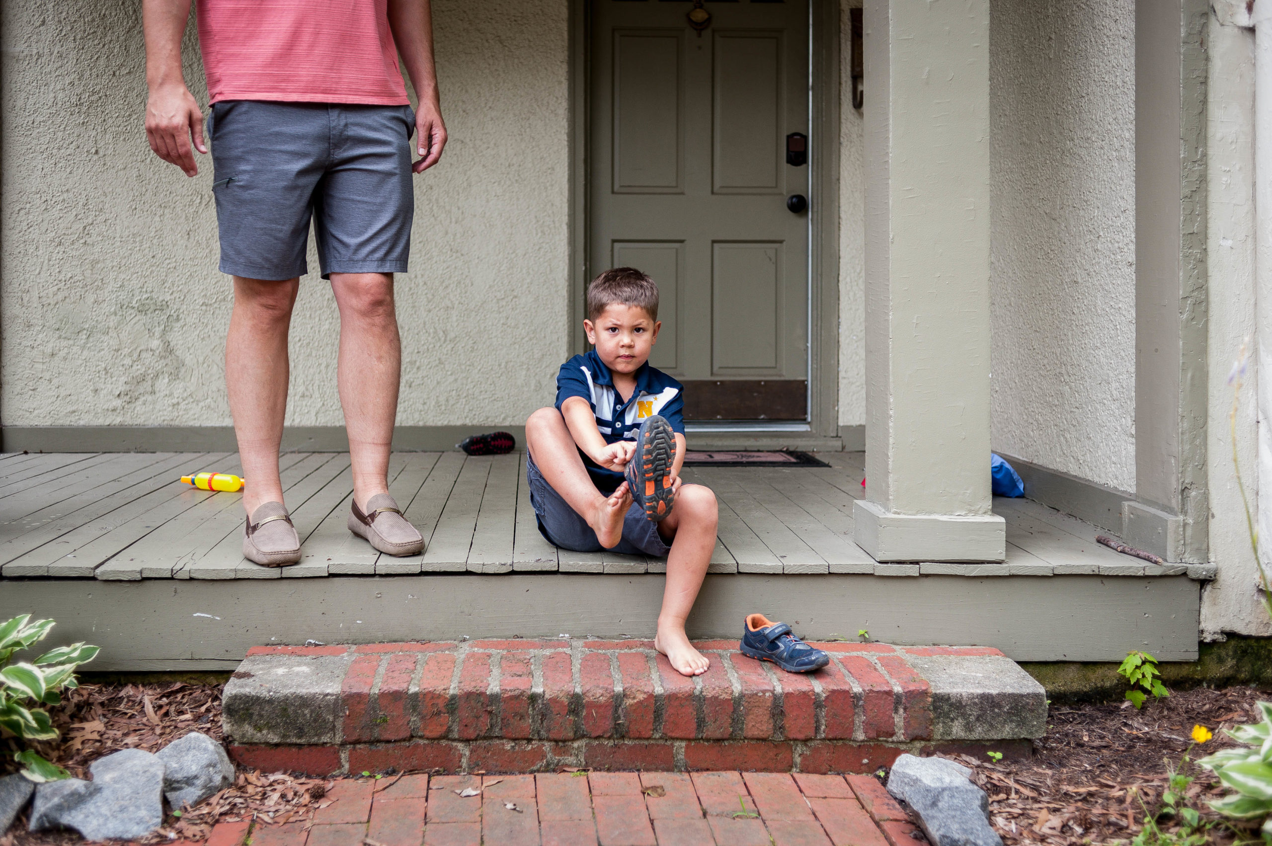 Boy sits on front porch to put on shoes during family photo session in williamsburg.