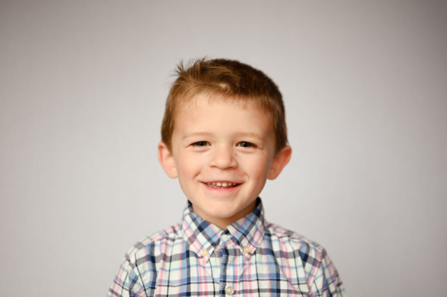 Little boy wearing plaid smiles for school photographer, Dreama Spence.