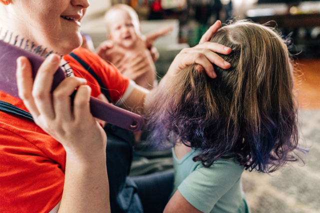 Mama uses a purple brush to get out tangles in daughters curly purple tip-dyed hair.