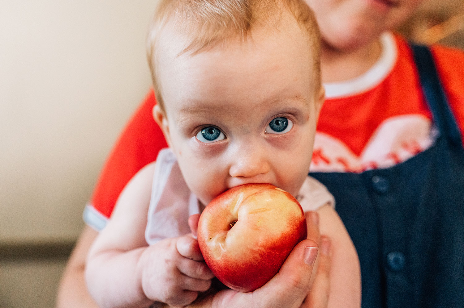 a close up of a mom holding a baby who is nibbling on a peach.