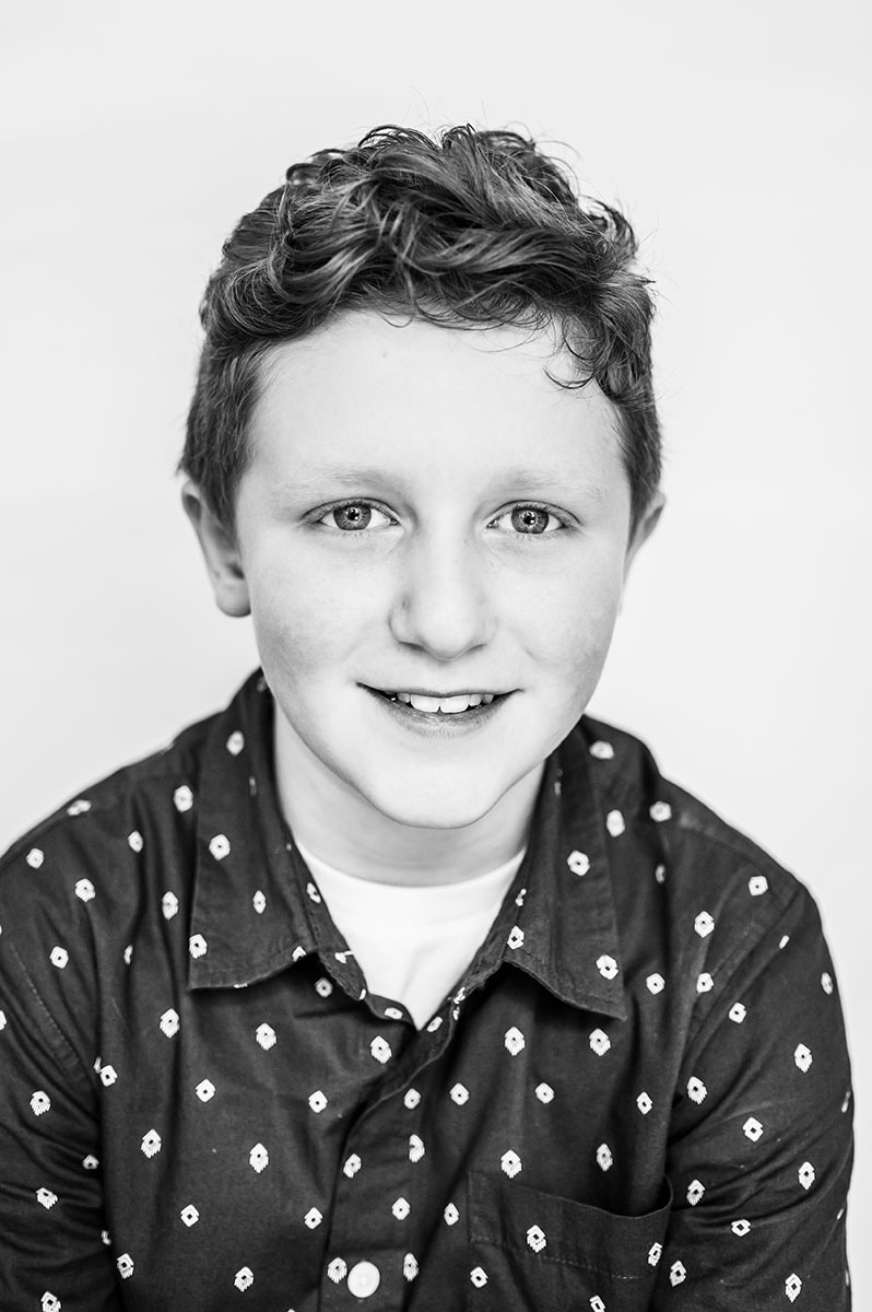 web-Hampton-Roads-Unschooled-Portrait-photographer-Dreama-Spence-4878-2 a black and white portrait of a boy with curly hair, a smile, and a dark shirt with a small white pattern one it.