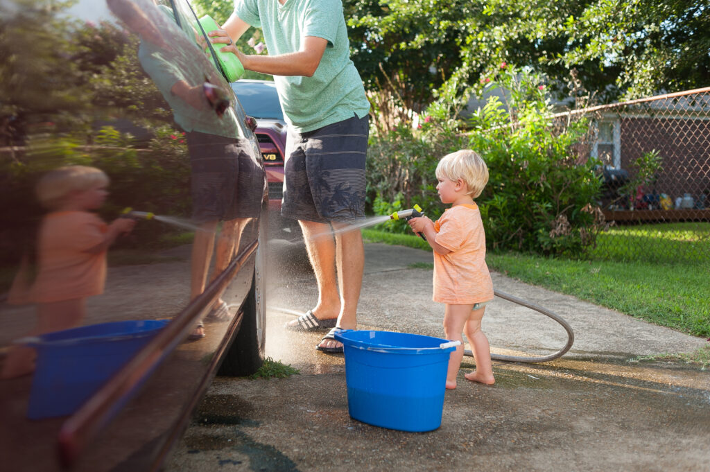 a toddler wearing a orange shirt and wearing a diaper helps his dad was the car