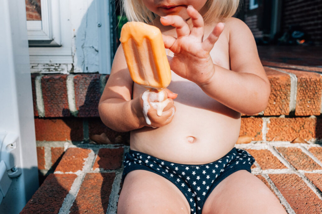 a little girl sits on the steps in her undies with a dreamcicle ice cream melting down her hand.