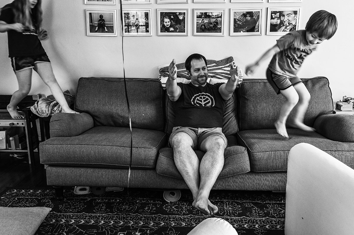Jerry holds his arms out while Emmet and Olivia try to jump over them on the couch of their Newport News, Virginia home.