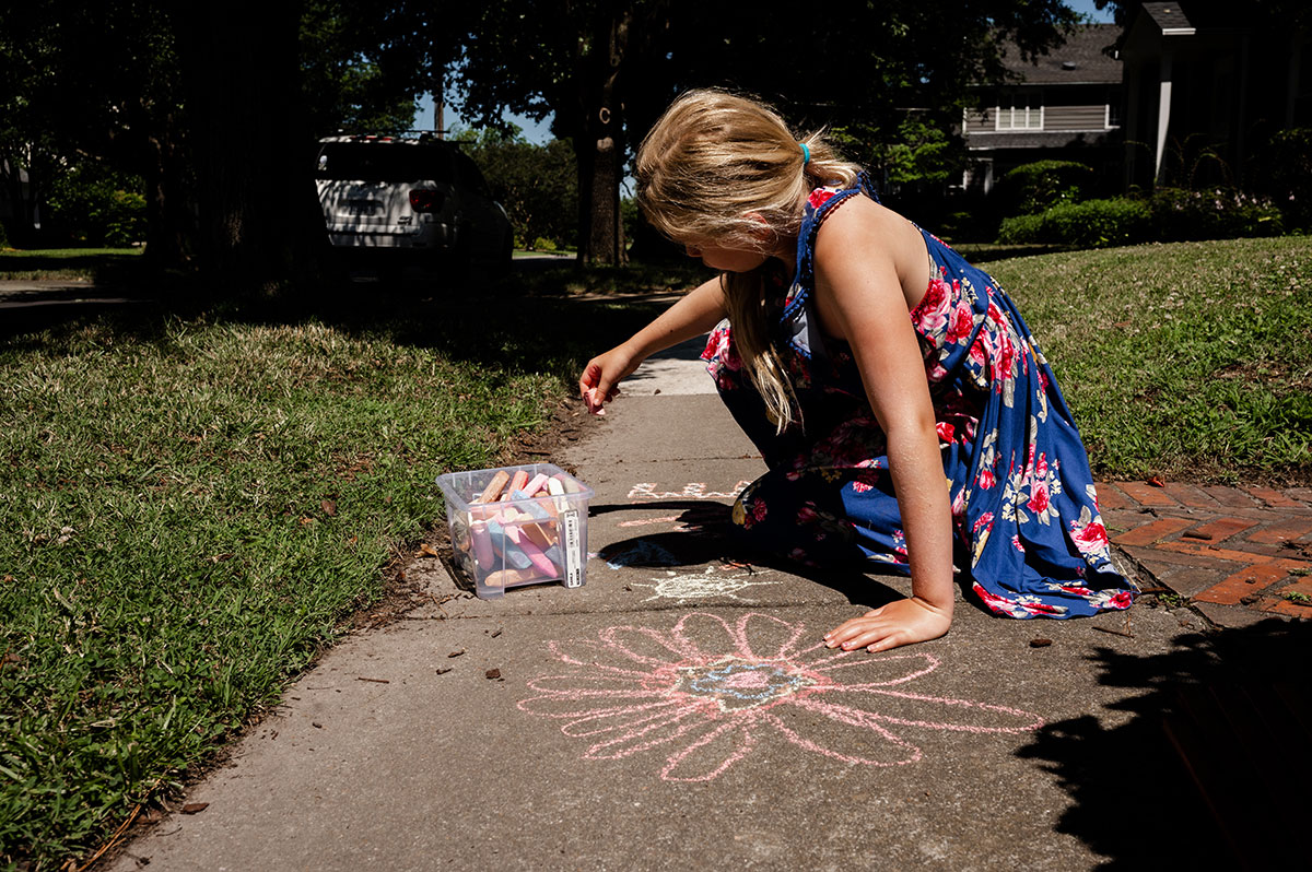 Piper draws flowers on the sidewalk in front of her home during a warm fall day.