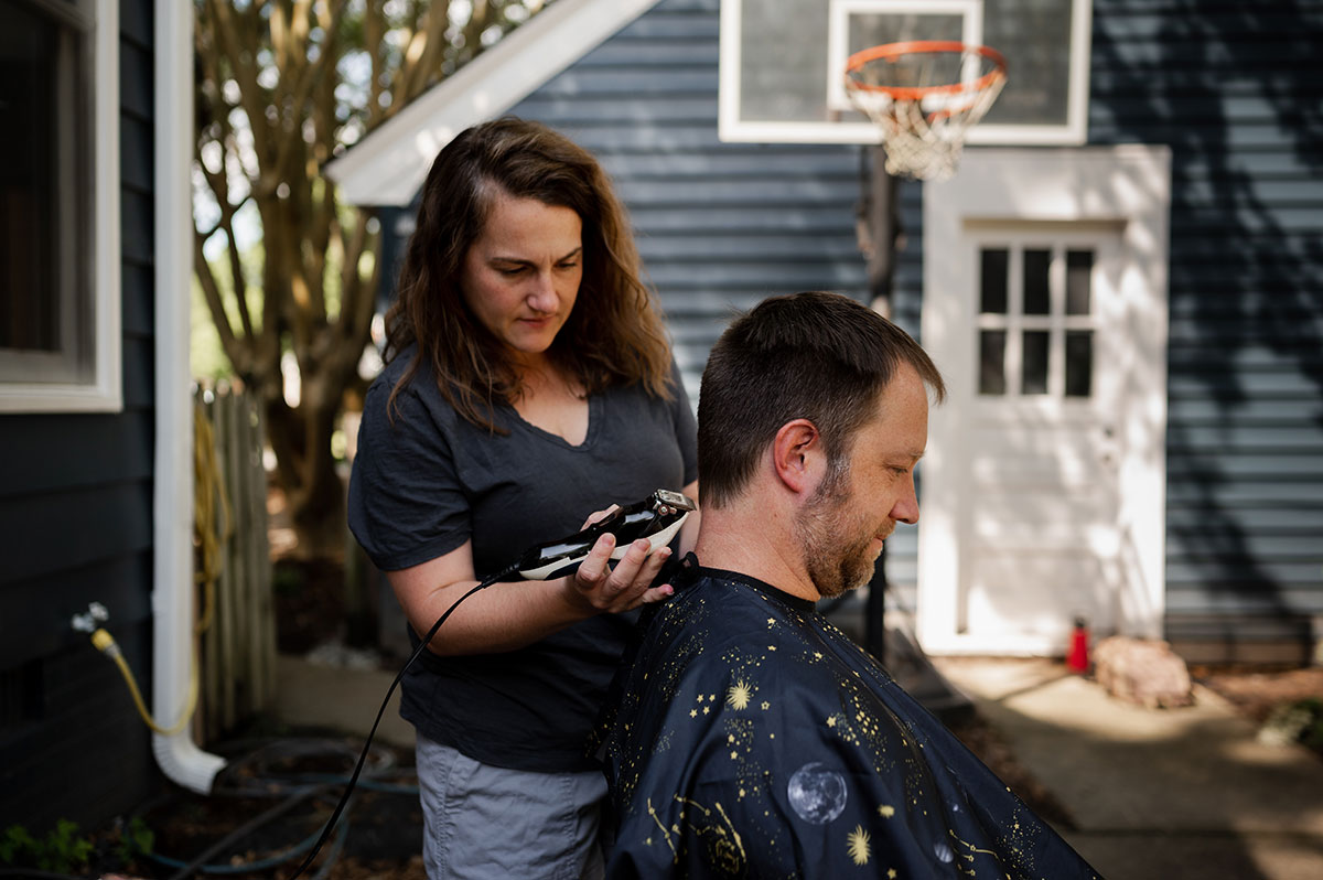 Wife gives husband a haircut outside during family session.