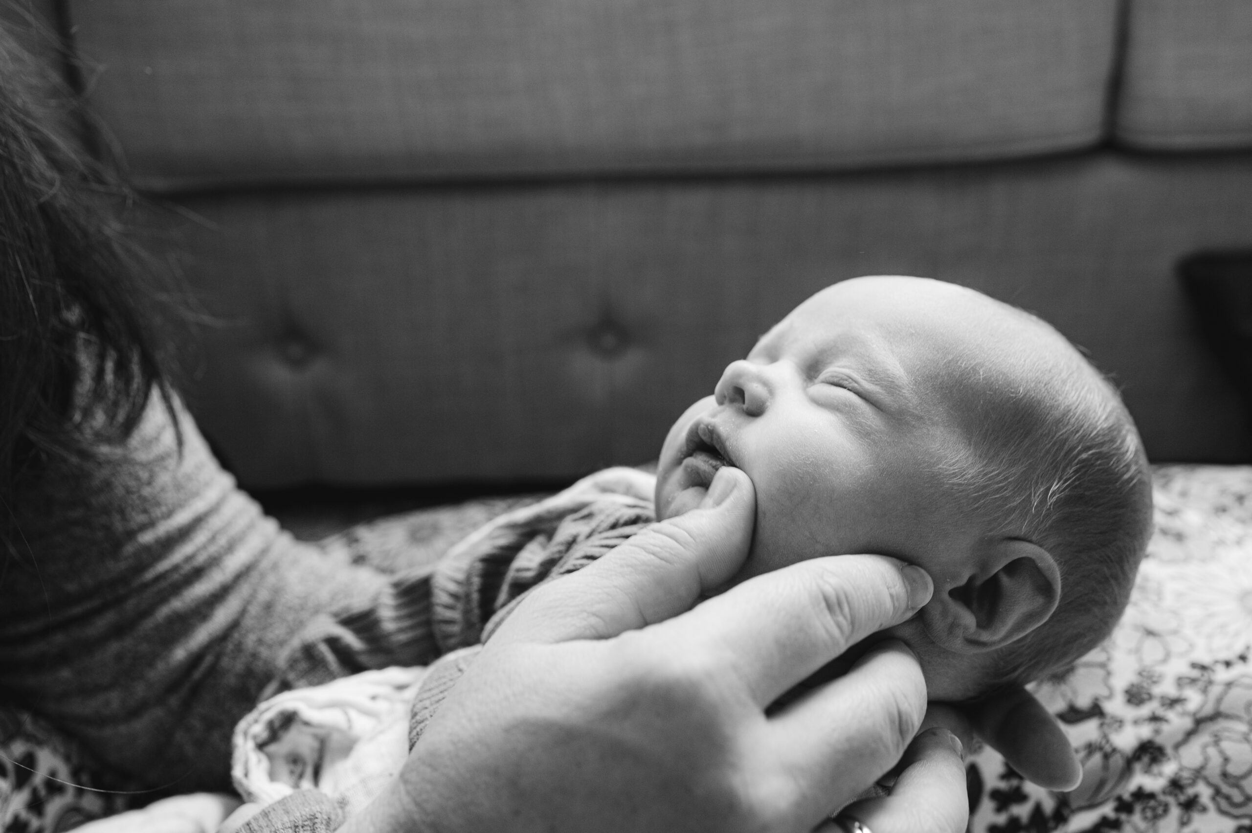 Mom wipes dried milk from newborns face during in-home lifestyle photography session.