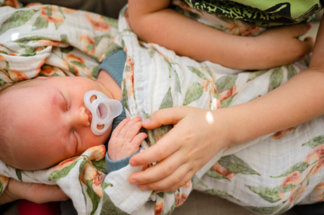 Big brother caresses baby sister during in-home newborn session.