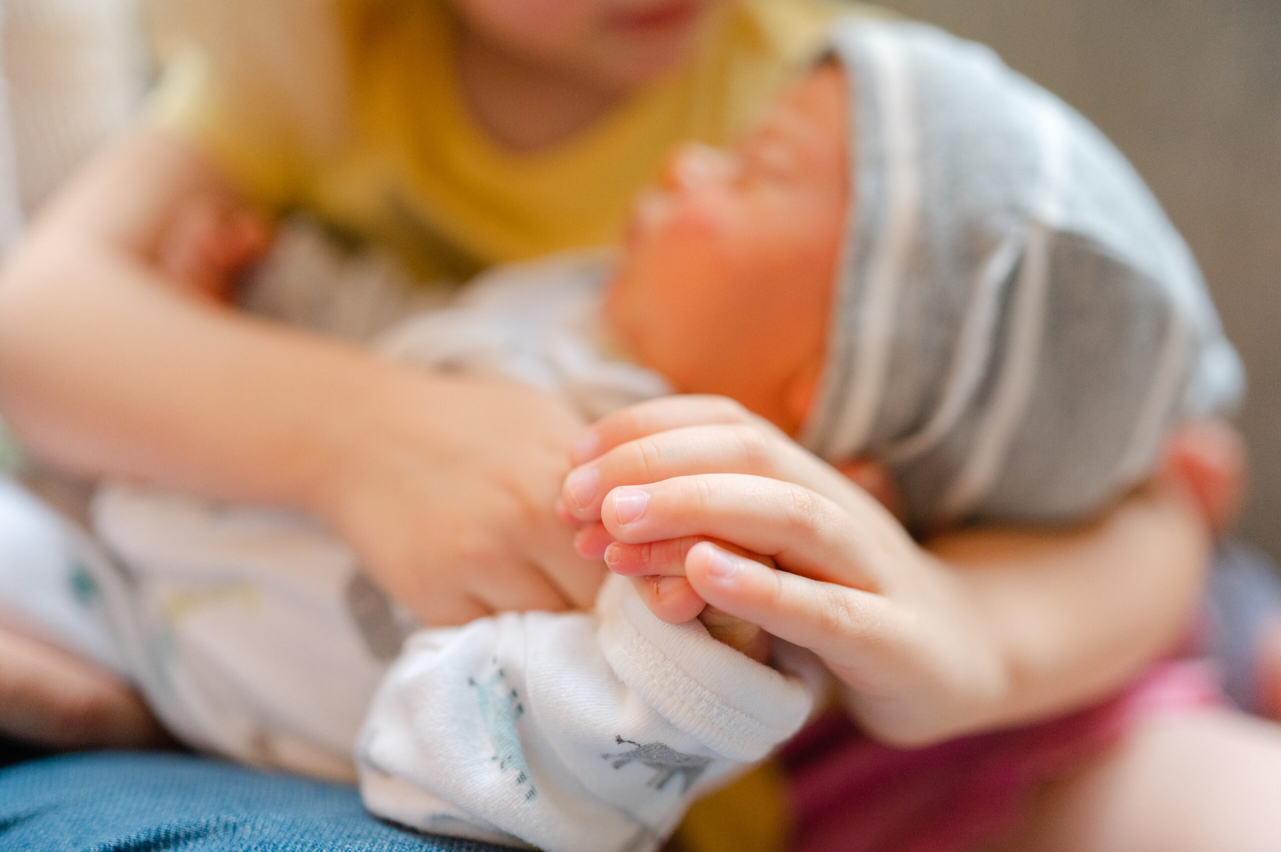 Big sister holds newborn brothers hand.