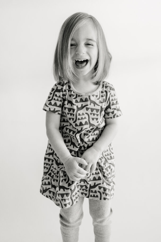 Black and white image of a girl laughing during her preschool portrait.