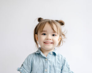 Little girl with top knot buns smiles at the camera for picture day.