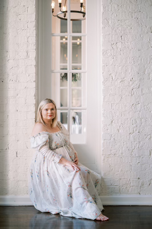 Photograph of Brielle sitting in a window wearing a dress.