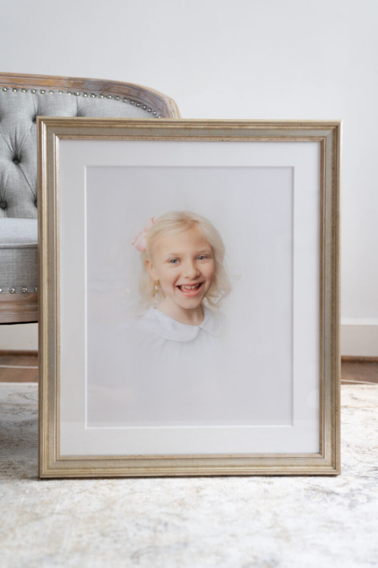 A golden framed print of a girl with a bow and white shirt.