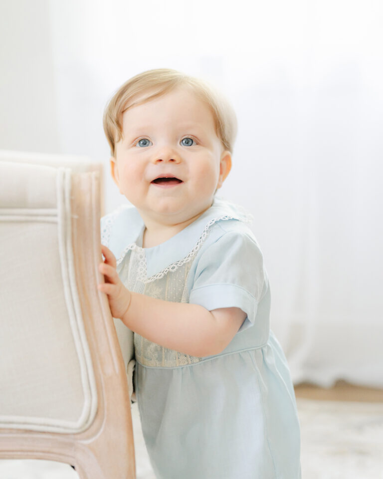 Little boy stands beside chair during his photo session.