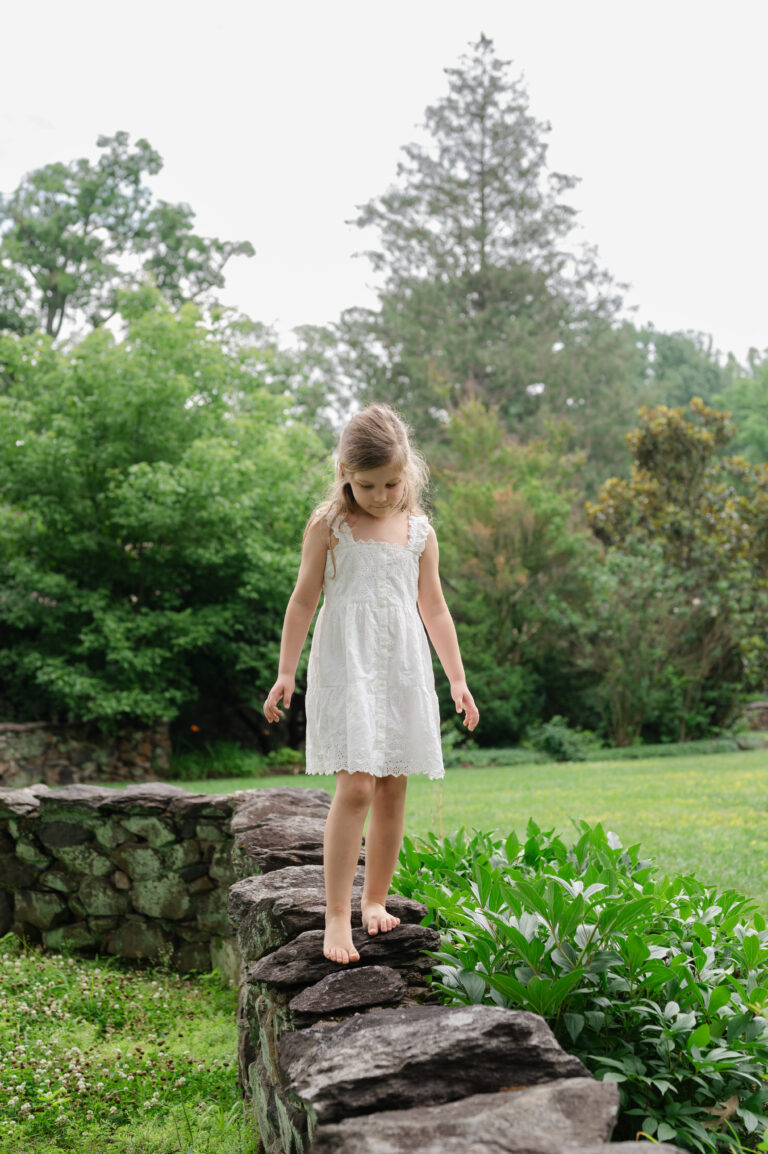 Girl walks along stone wall during family session in Williamsburg, Virginia.