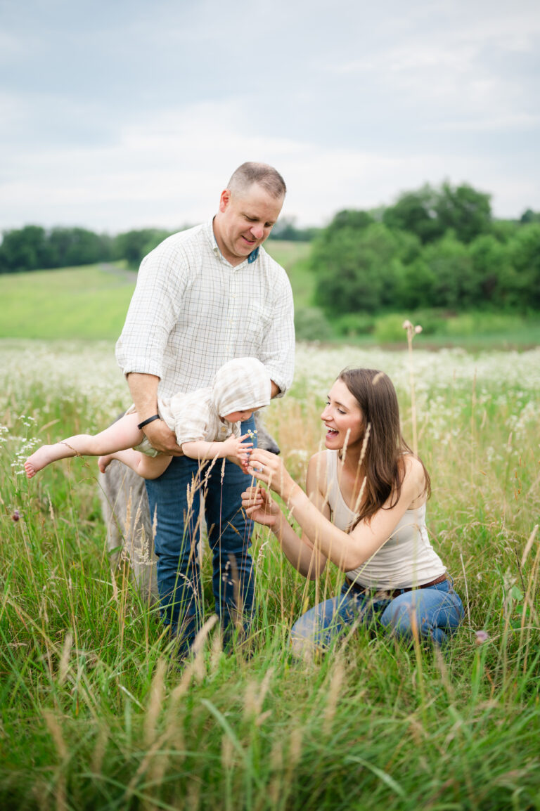Dad swings daughter in tall grass.