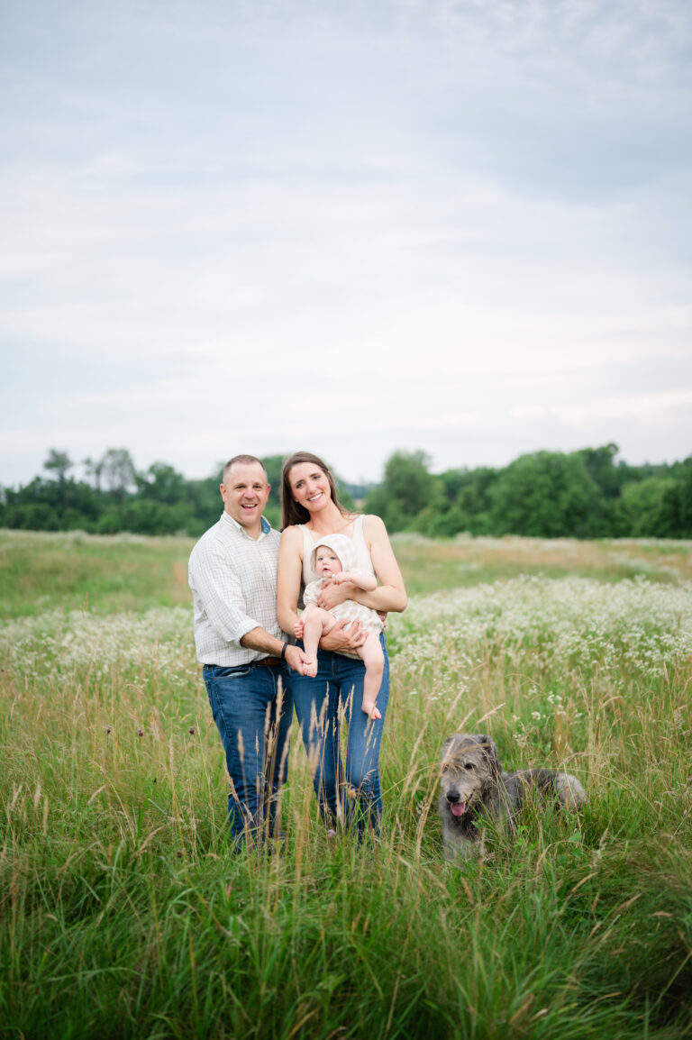 Mom, dad, toddler and family daog pose in tall grass in Yorktown, Virginia.
