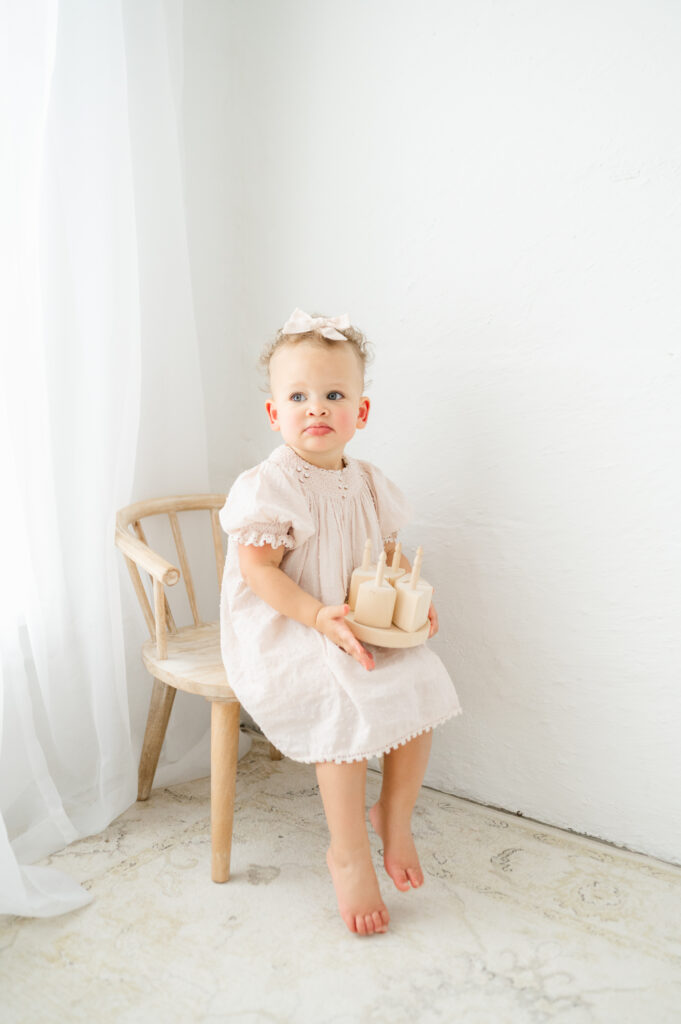 Baby girl playing with a wooden birthday cake during her first birthday milestone portraits.