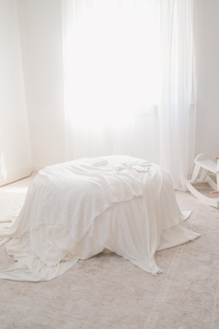 Soft white linens and newborn wardrobe prepared for a baby-led portrait session in the studio.