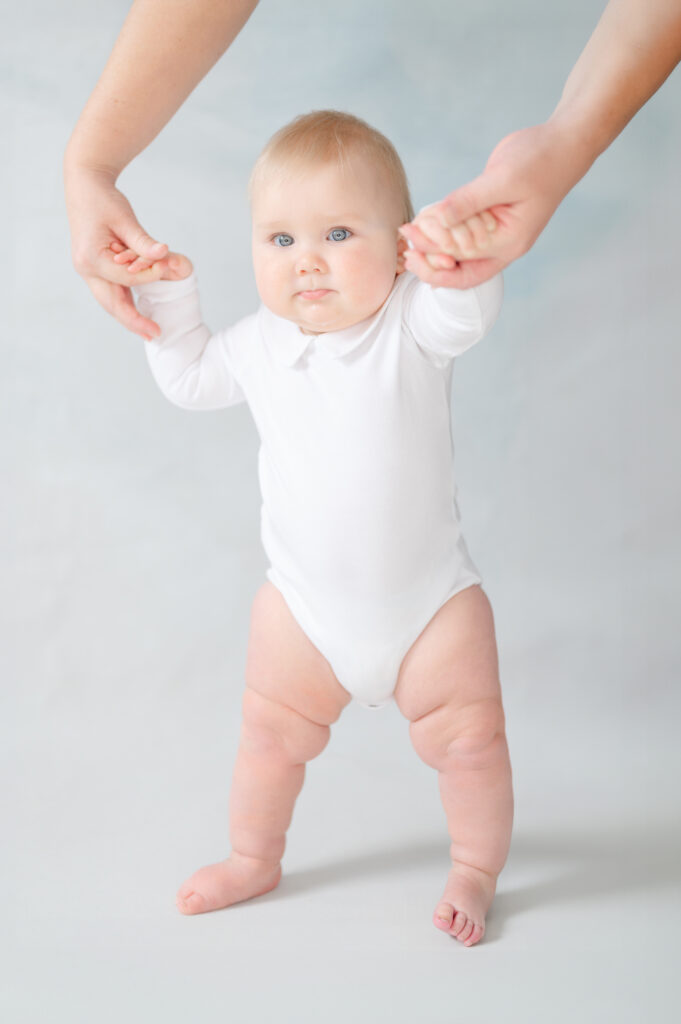Six-month-old baby boy smiling in a white Peter Pan outfit during a milestone photography session.